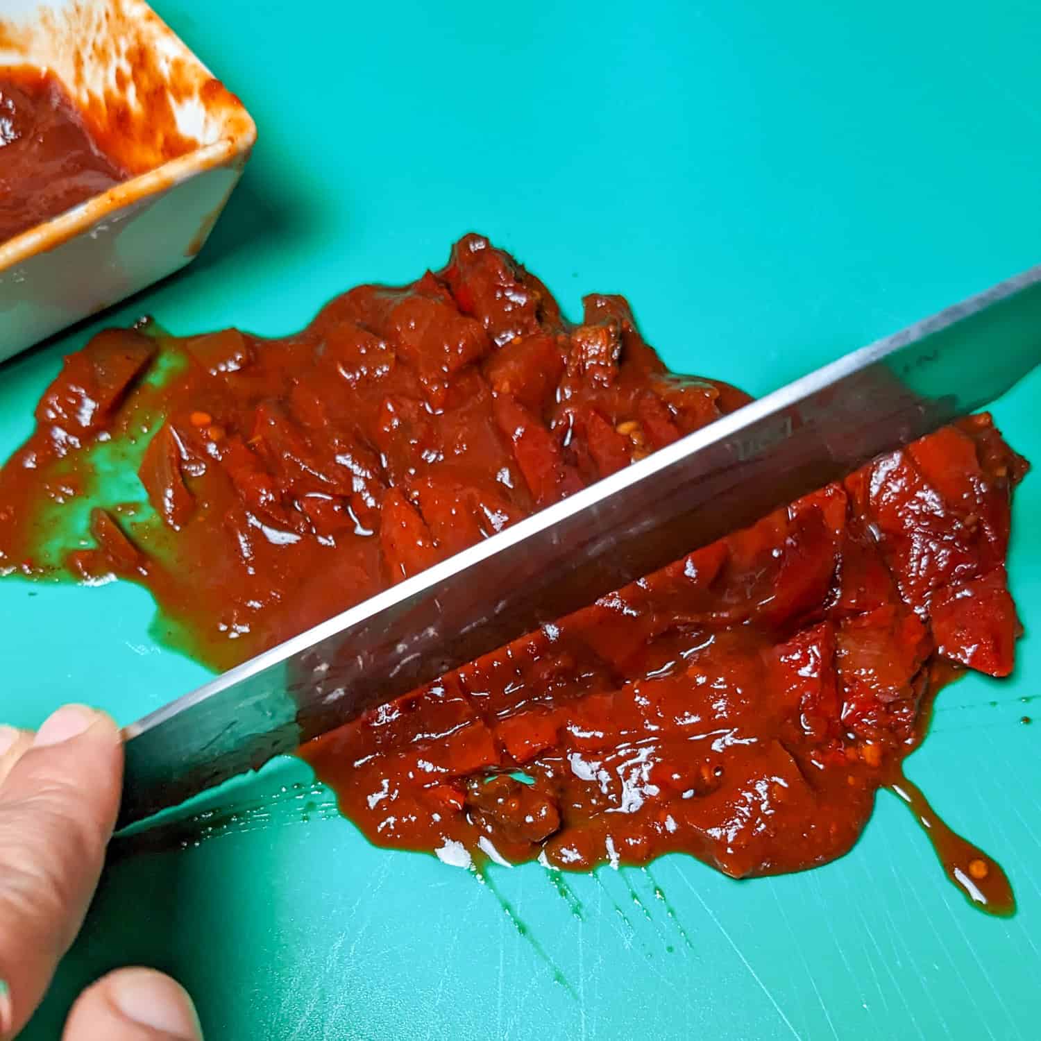 Chipotle in Adobo is being chopped on a green plastic cutting board.